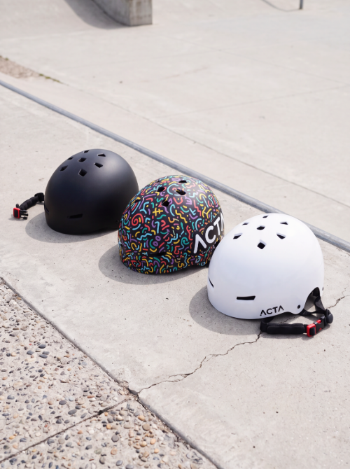 Trois casques ACTA Motion noir, Color Pop et blanc posés au sol dans un skatepark