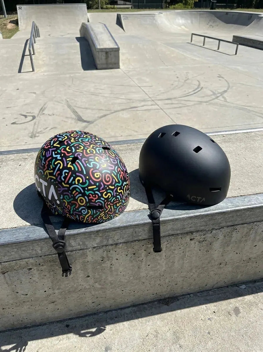Casques ACTA — motif multicolore et noir mat, posés sur un skatepark