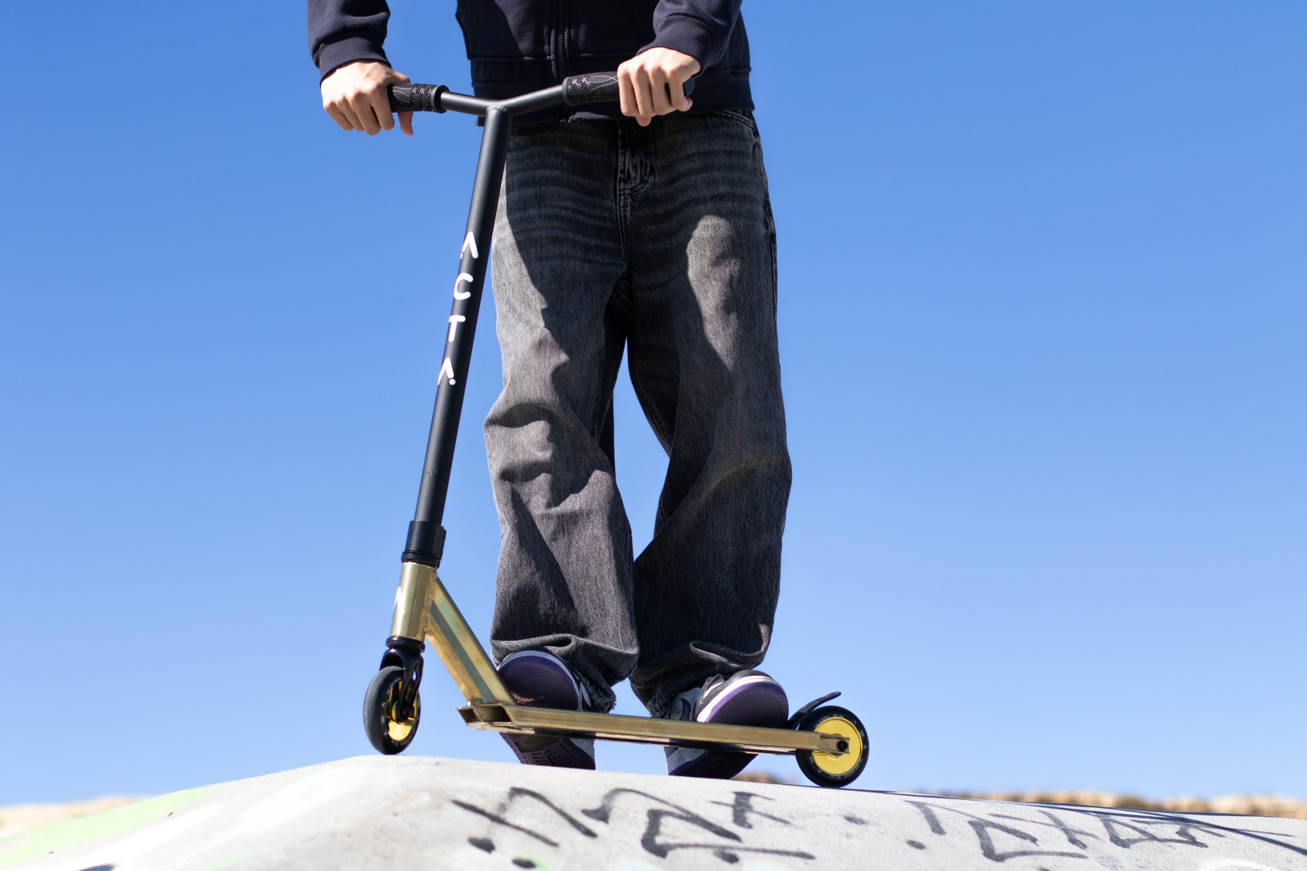 Trottinette freestyle ACTA KSP Gold — rider immobile, debout en haut d'un module de skatepark