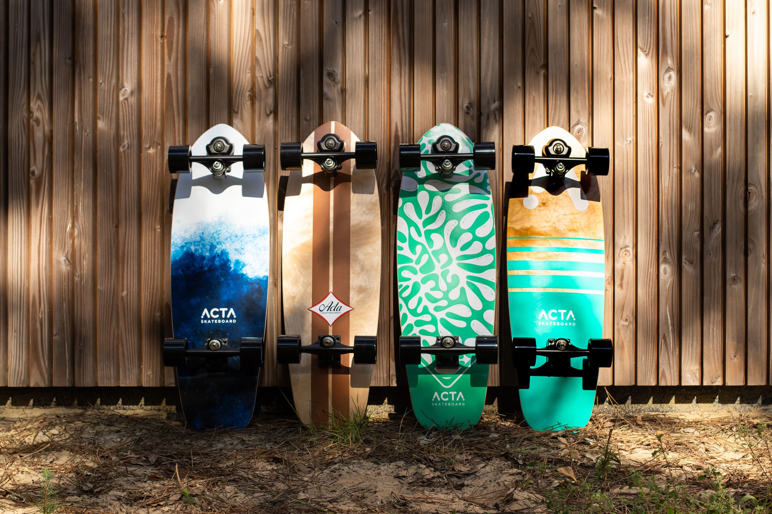 Quatre surfskates ACTA appuyés contre une palissade en bois